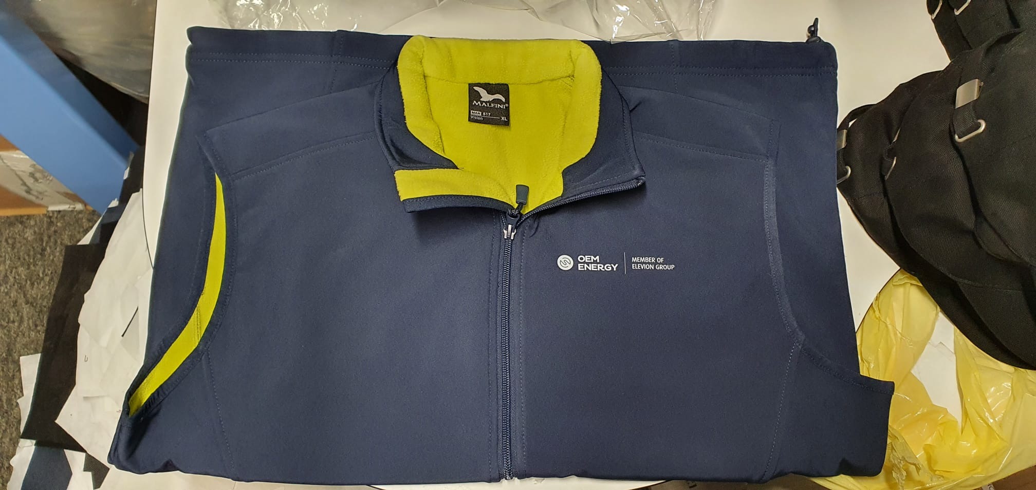 Granatowa bluza robocza z żółtymi wstawkami i logo OEM Energy oraz Eleven Group, leżąca na stole.