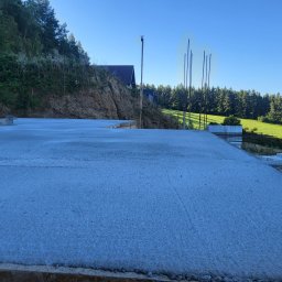 BORYSBUD Natan Borysiewicz - Wylana płyta fundamentowa z wystającymi prętami zbrojeniowymi na tle zieleni w Nowej Rudzie. Widok na wzgórze i las.