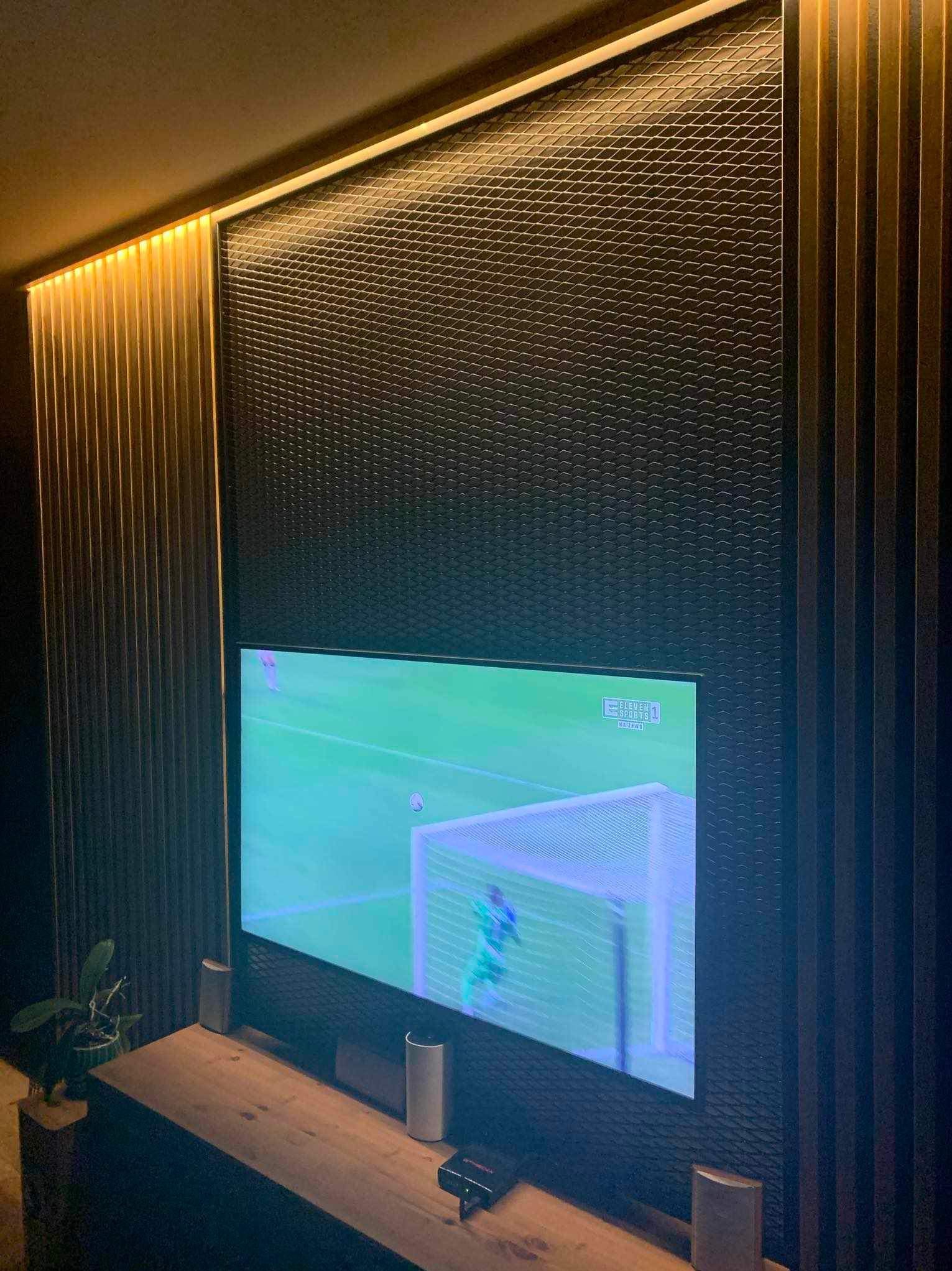 Nowoczesny salon z telewizorem wkomponowanym w ścianę z dekoracyjną, podświetlaną boazerią i panelem 3D. Minimalistyczny design, ciepłe oświetlenie.