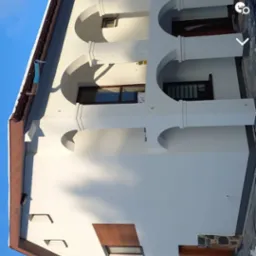 Świeżo pomalowana elewacja budynku z charakterystycznymi łukami, widoczna drabina oparta o ścianę, brązowe okna i dach, zimowy krajobraz w tle.