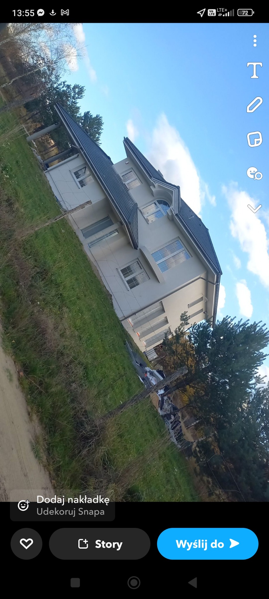 Nowoczesny dom jednorodzinny z szarym dachem, widok z dołu, fragment zarośniętego trawnika i porozrzucane materiały budowlane w tle.