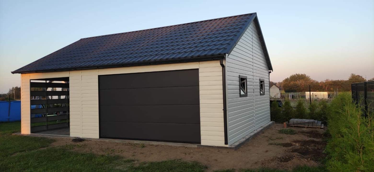 Nowoczesny garaż z blachy trapezowej w kolorze kremowym i szarym, z czarną bramą segmentową i dachem dwuspadowym z blachodachówki, widok z zewnątrz na tle zieleni.