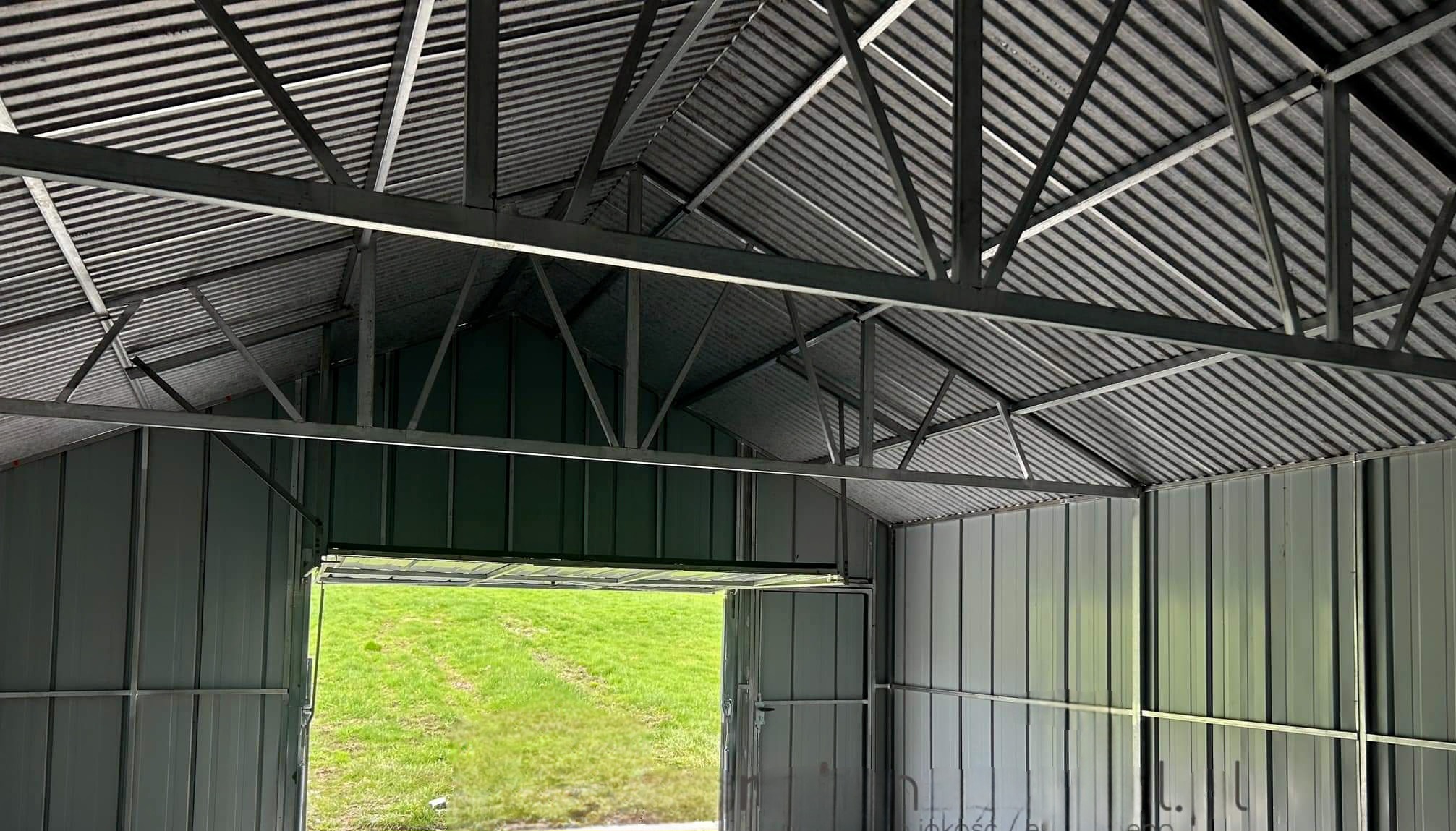 Wnętrze szkieletu metalowego garażu blaszanego z widokiem na zielony trawnik w Bratysławie, konstrukcja dachu z blachy falistej i stalowych belek.