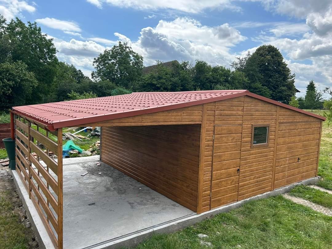 Nowoczesny garaż blaszany z zadaszeniem i drewnianą konstrukcją, pomalowany na brązowo, z czerwoną blachodachówką, na betonowej wylewce, otoczony zielenią.