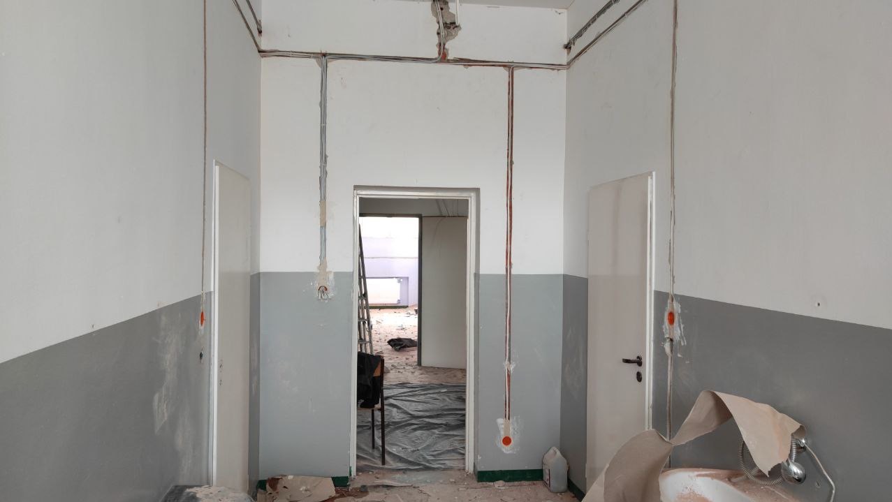 Wnętrze w trakcie remontu z widocznymi przewodami elektrycznymi prowadzonymi po ścianach, zabezpieczona folią podłoga i drabina w przejściu.