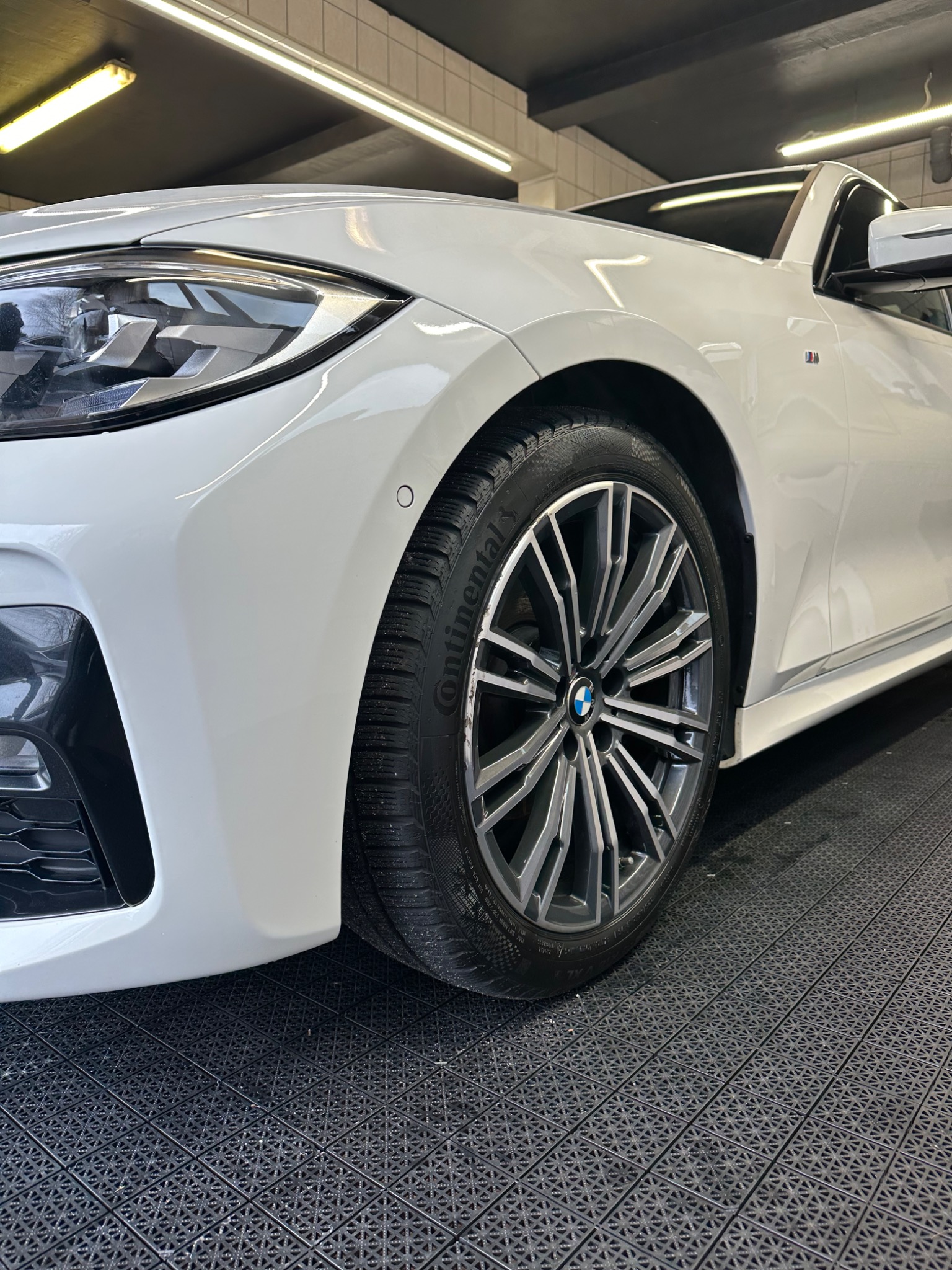 Biały samochód BMW z oponami Continental, widoczny z bliska w myjni, na czarnej podłodze z kratką