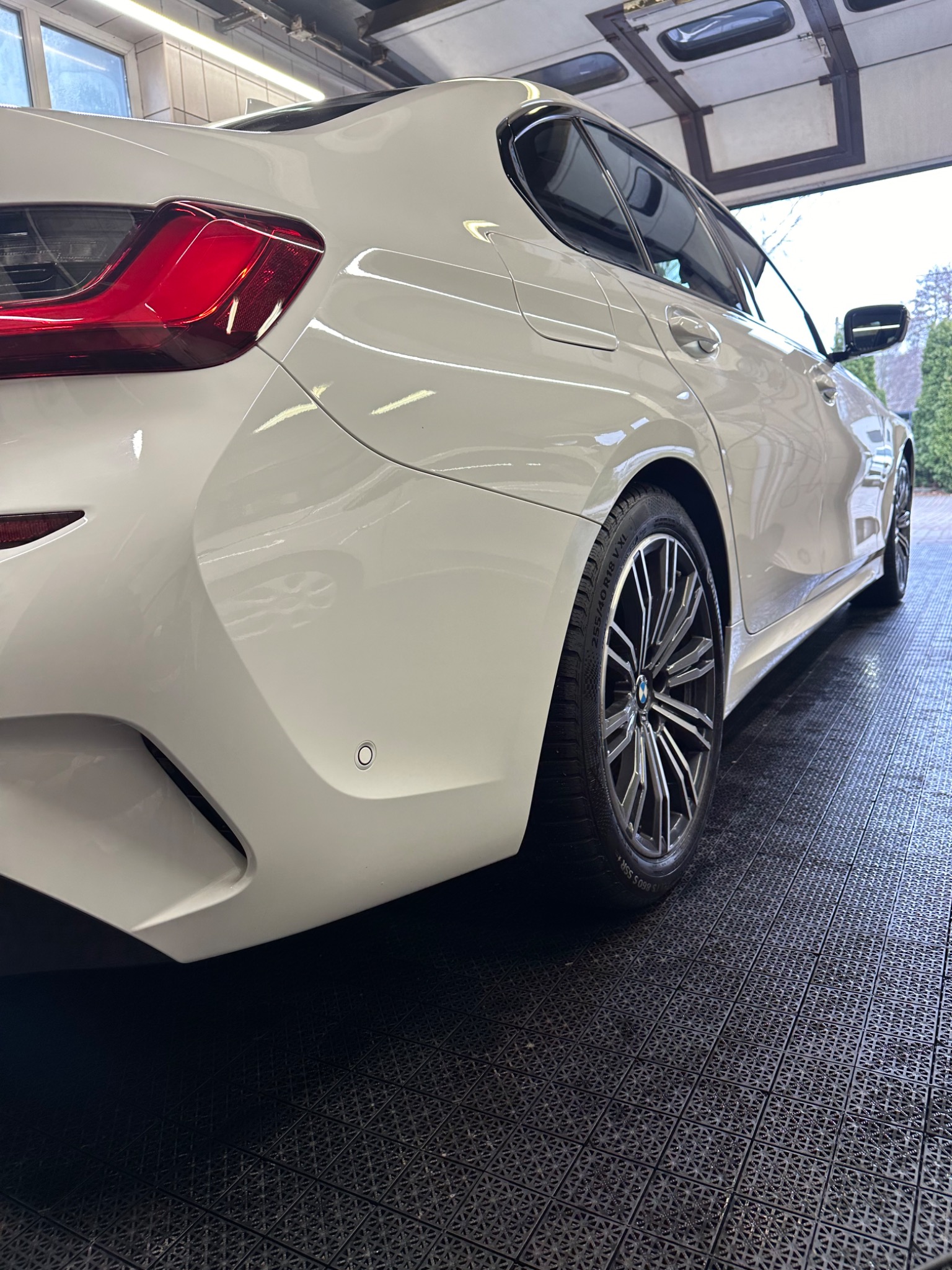 Biała, lśniąca karoseria samochodu BMW, widok z tyłu, po dokładnym umyciu, na czarnej, gumowej podłodze myjni.