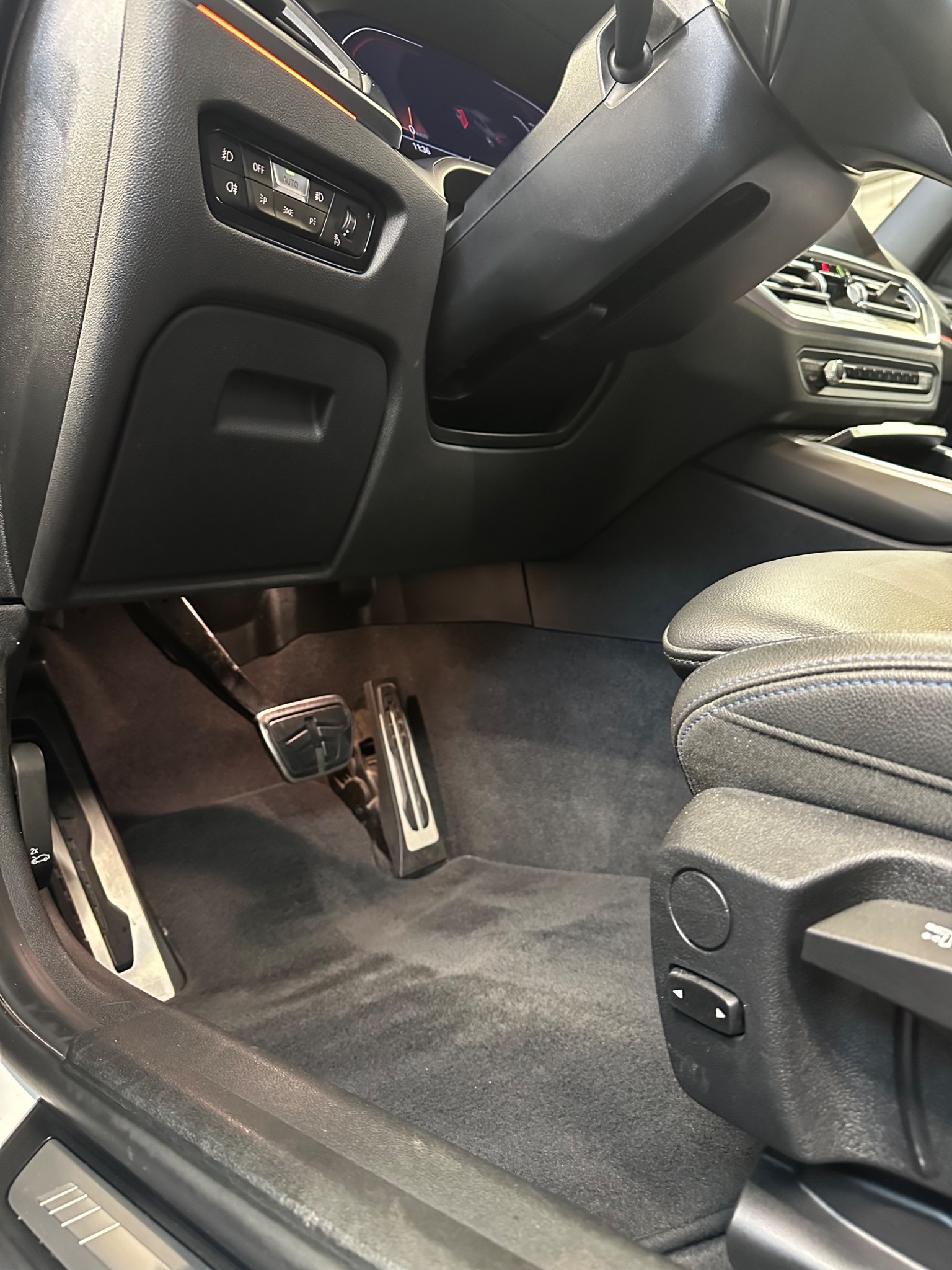 Wnętrze samochodu z widocznymi pedałami, dywanikami i fragmentem skórzanego fotela z niebieską nicią, po czyszczeniu.