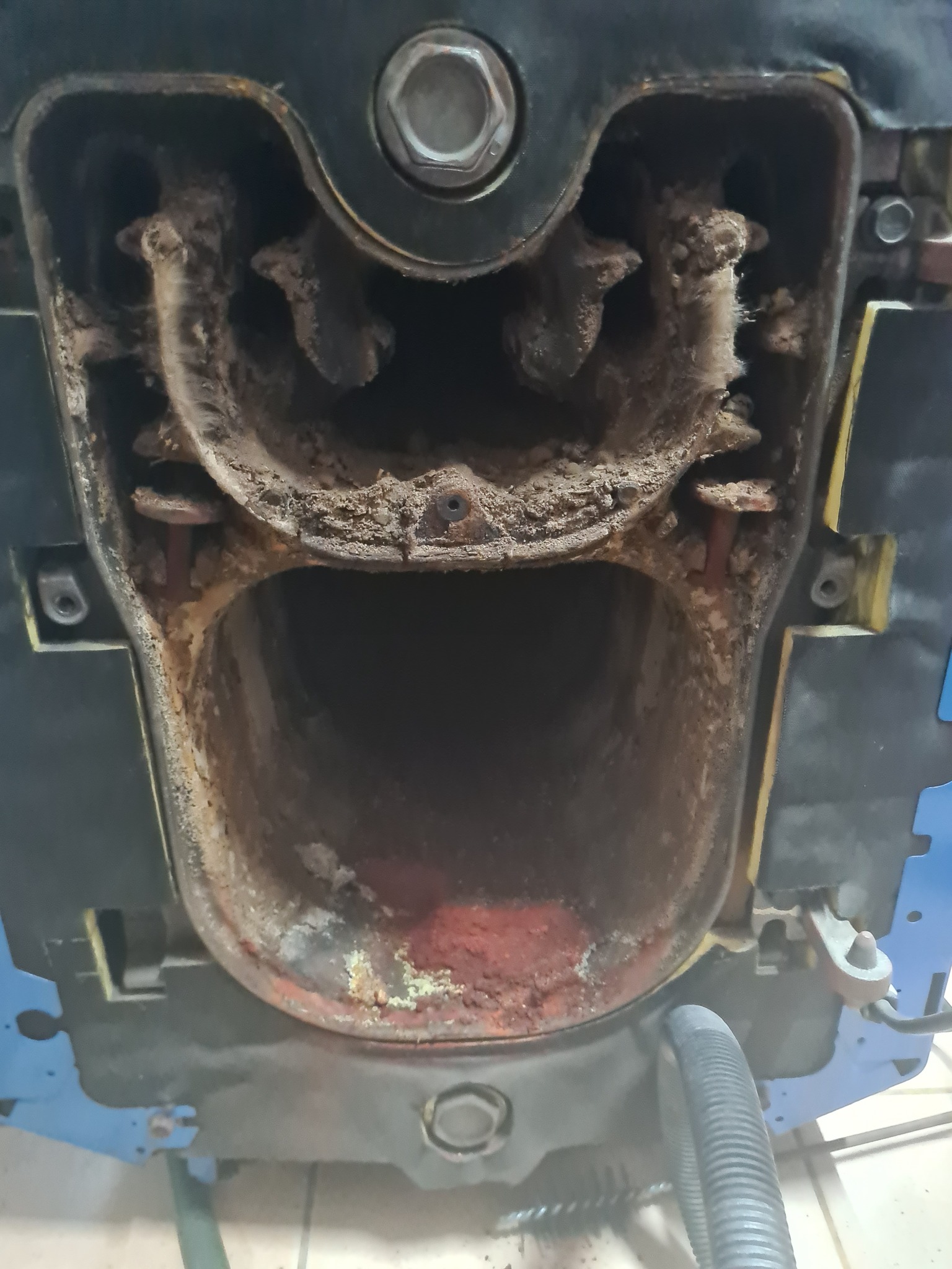 Wnętrze otwartego, zanieczyszczonego kotła gazowego z widocznymi osadami i korozją, czyszczone wężem odkurzacza przemysłowego.