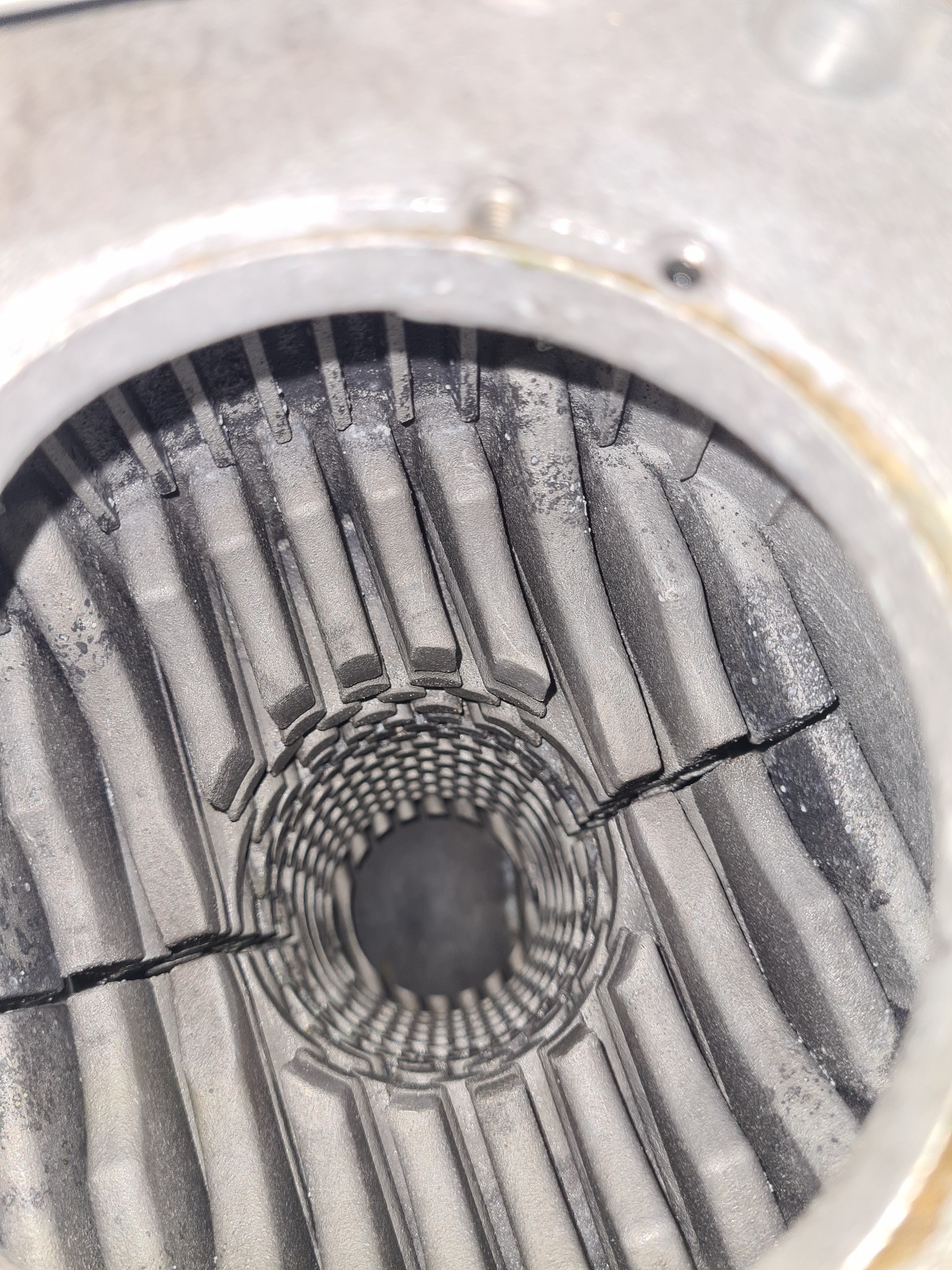 Wnętrze pieca gazowego z widocznymi elementami grzewczymi pokrytymi osadem, widok z bliska na żeliwne żeberka wymiennika ciepła.