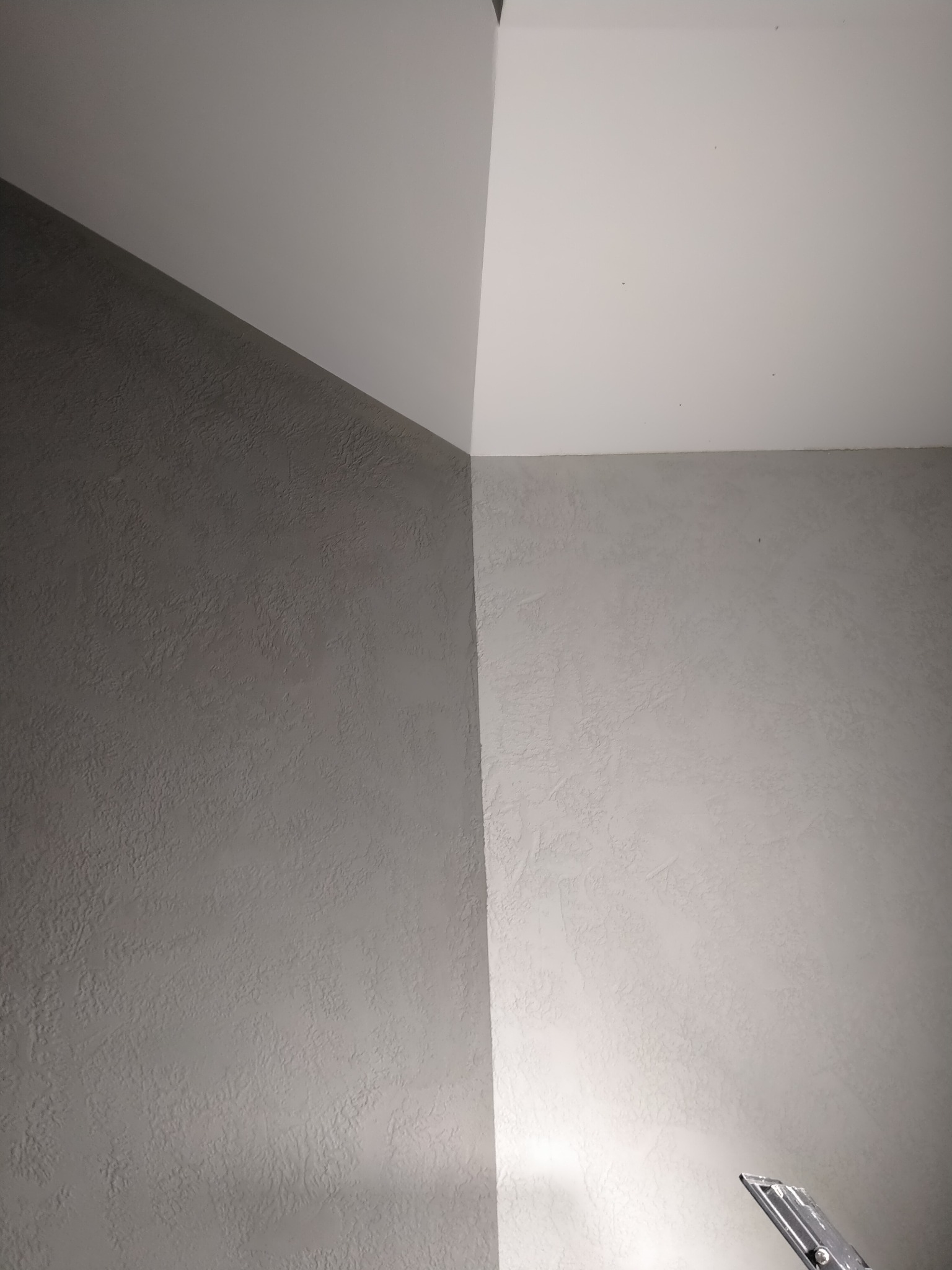 Ściana wewnętrzna pokryta tynkiem strukturalnym w dwóch odcieniach szarości, z widocznym fragmentem narzędzia malarskiego w prawym dolnym rogu.
