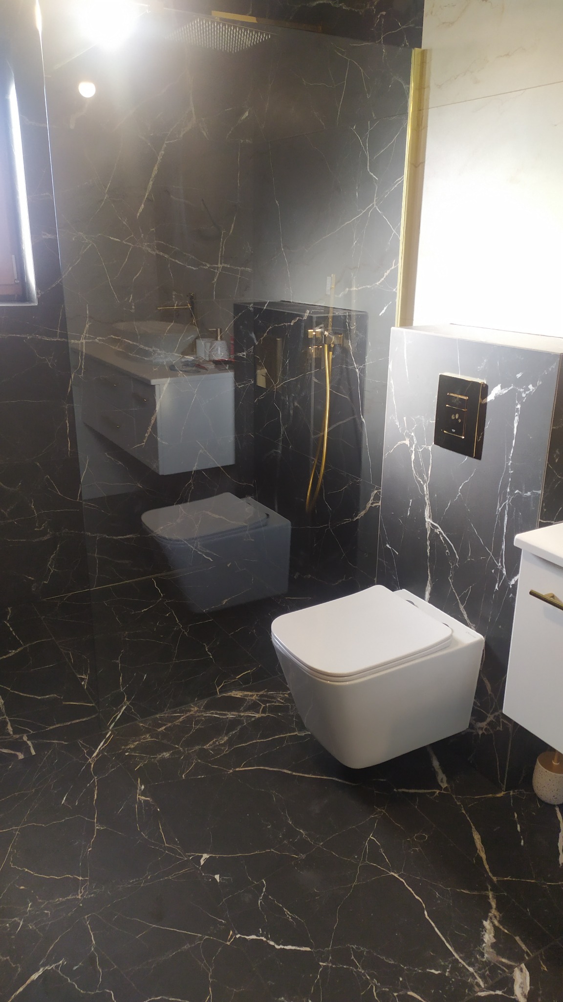 Nowoczesna łazienka w Wołominie z czarnymi marmurowymi płytkami, podwieszana toaleta i złota armatura.
