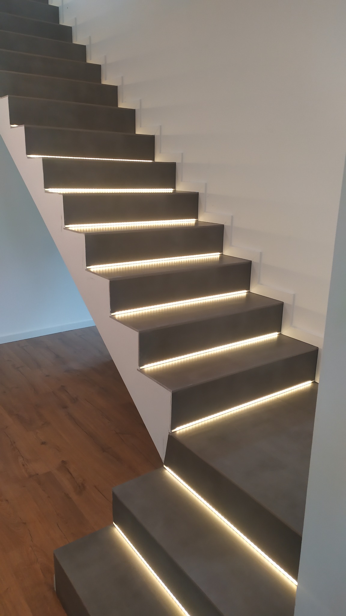 Nowoczesne schody betonowe z podświetleniem LED, widok z dołu, minimalistyczny design, drewniana podłoga w tle.