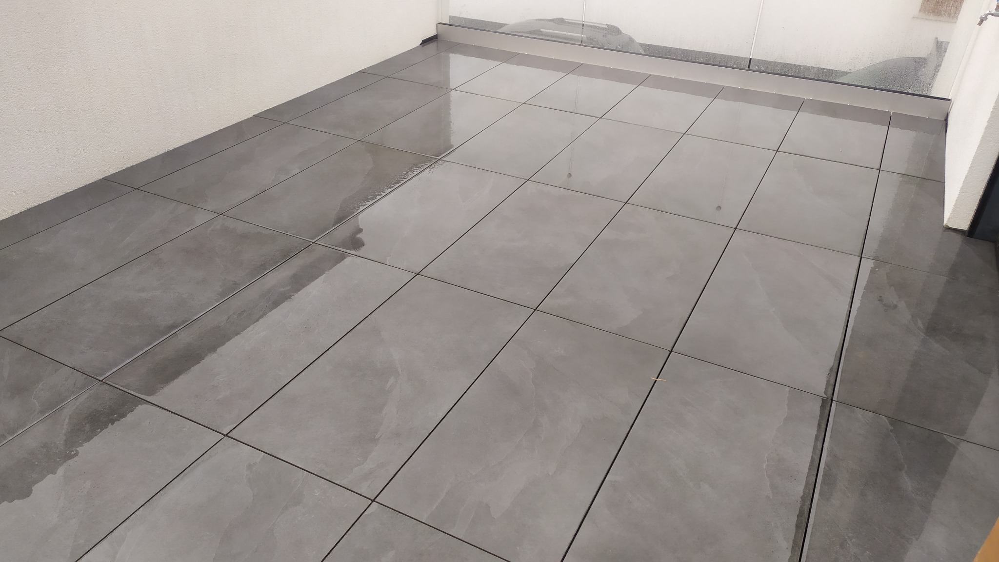 Błyszczące, szare płytki gresowe na podłodze balkonu, widoczne odbicia światła i fuga w ciemniejszym odcieniu.
