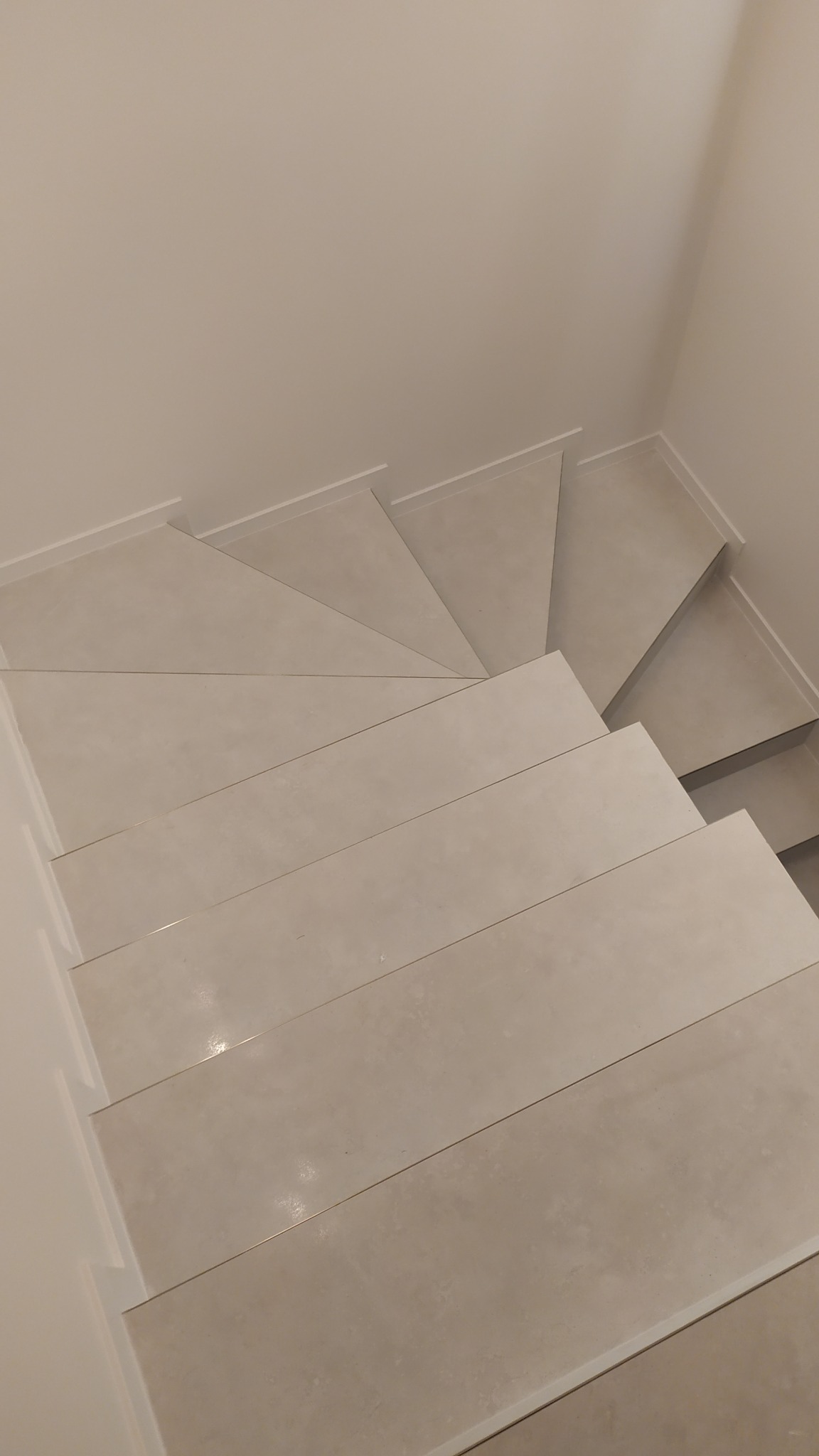 Schody wewnętrzne wykończone jasnymi, matowymi płytkami ceramicznymi, widok z góry, minimalistyczny design.