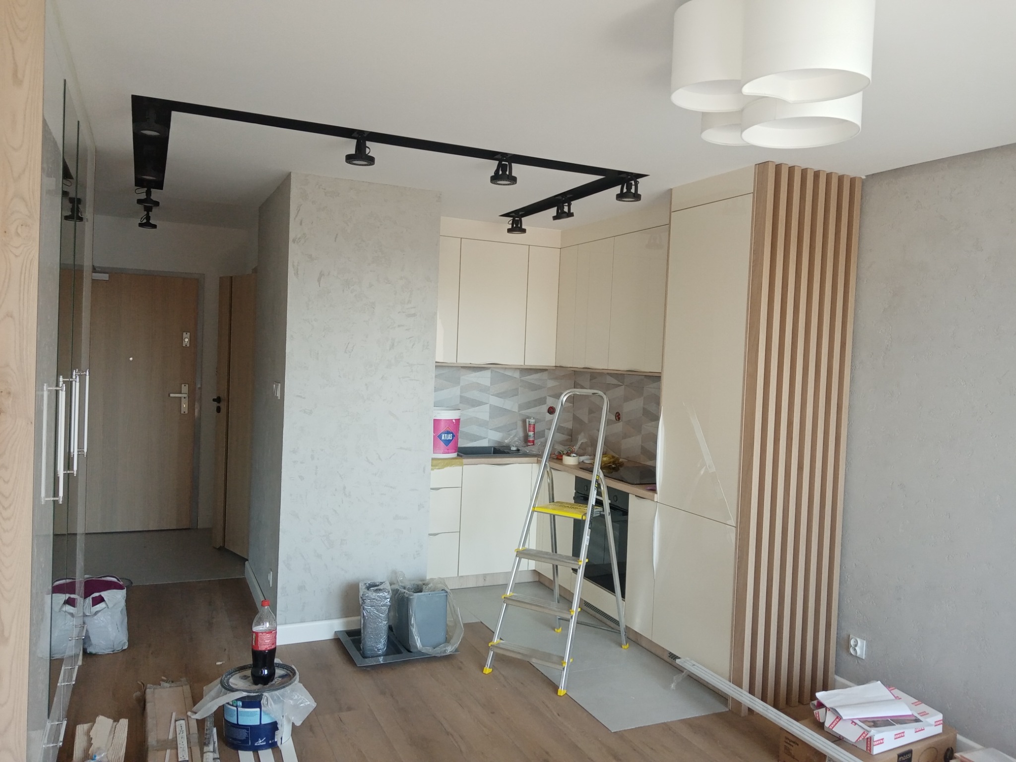 Nowoczesna kuchnia w trakcie remontu: drabina, puszki z farbą i narzędzia widoczne w pomieszczeniu z zamontowanym oświetleniem szynowym.