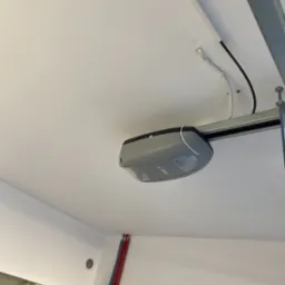 Zamontowany napęd do bramy garażowej CAME na szynie montażowej, widoczne przewody elektryczne i rury instalacyjne w tle.