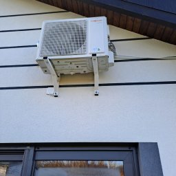 PHU Oskar - Biała jednostka zewnętrzna klimatyzacji marki Viessmann zamontowana na wspornikach na elewacji domu z widocznym oknem w dolnej części kadru.