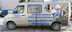 Srebrny samochód dostawczy z nadrukowaną reklamą firmy instalacyjnej, zawierającą hasła: technika grzewcza, stacje uzdatniania wody, fotowoltaika oraz zdjęcia urządzeń grzewczych i klimatyzacyjnych...