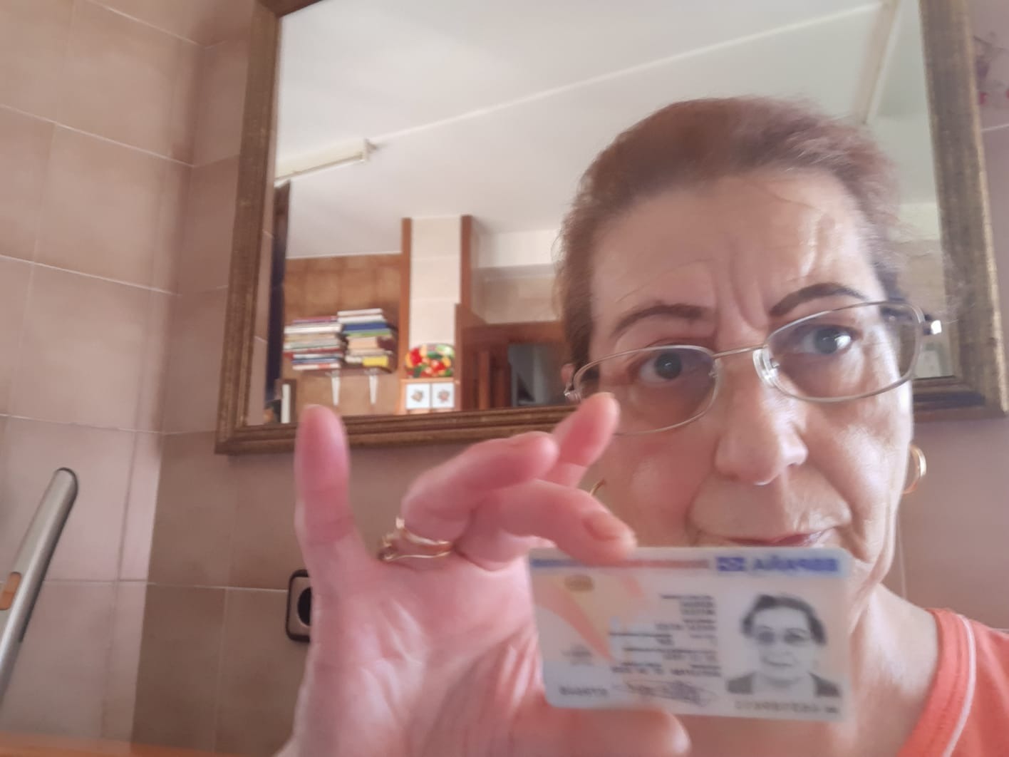 Osoba w okularach trzyma w dłoni dokument tożsamości na tle łazienki z lustrem.