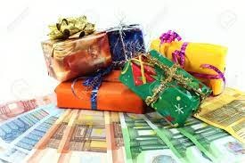 Stos prezentów w ozdobnych papierach i z kokardami, ułożony na wachlarzu banknotów różnej waluty.