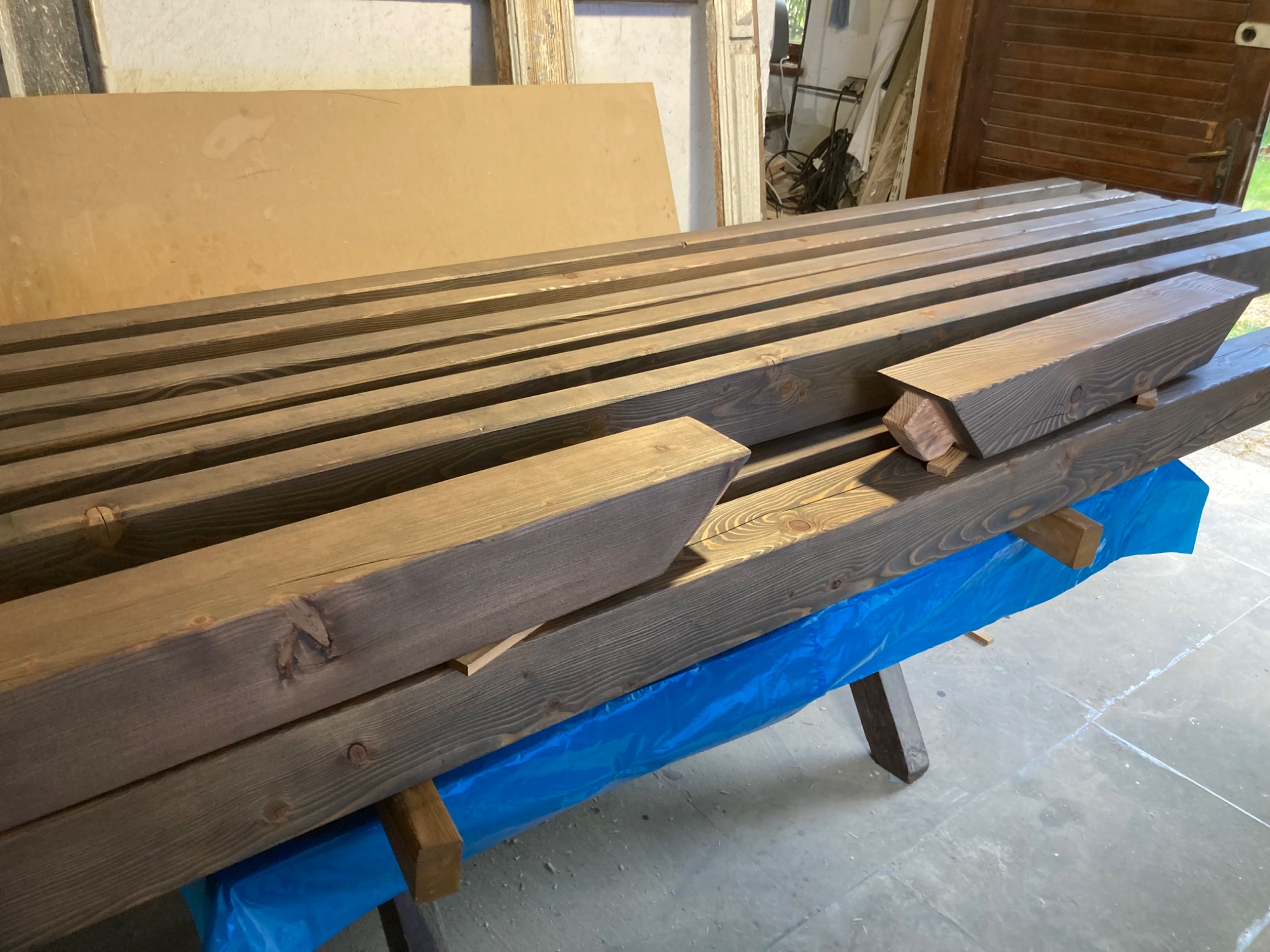 Przygotowane, impregnowane drewniane elementy konstrukcyjne z przyciętymi końcówkami, ułożone na stole roboczym zabezpieczonym folią malarską.