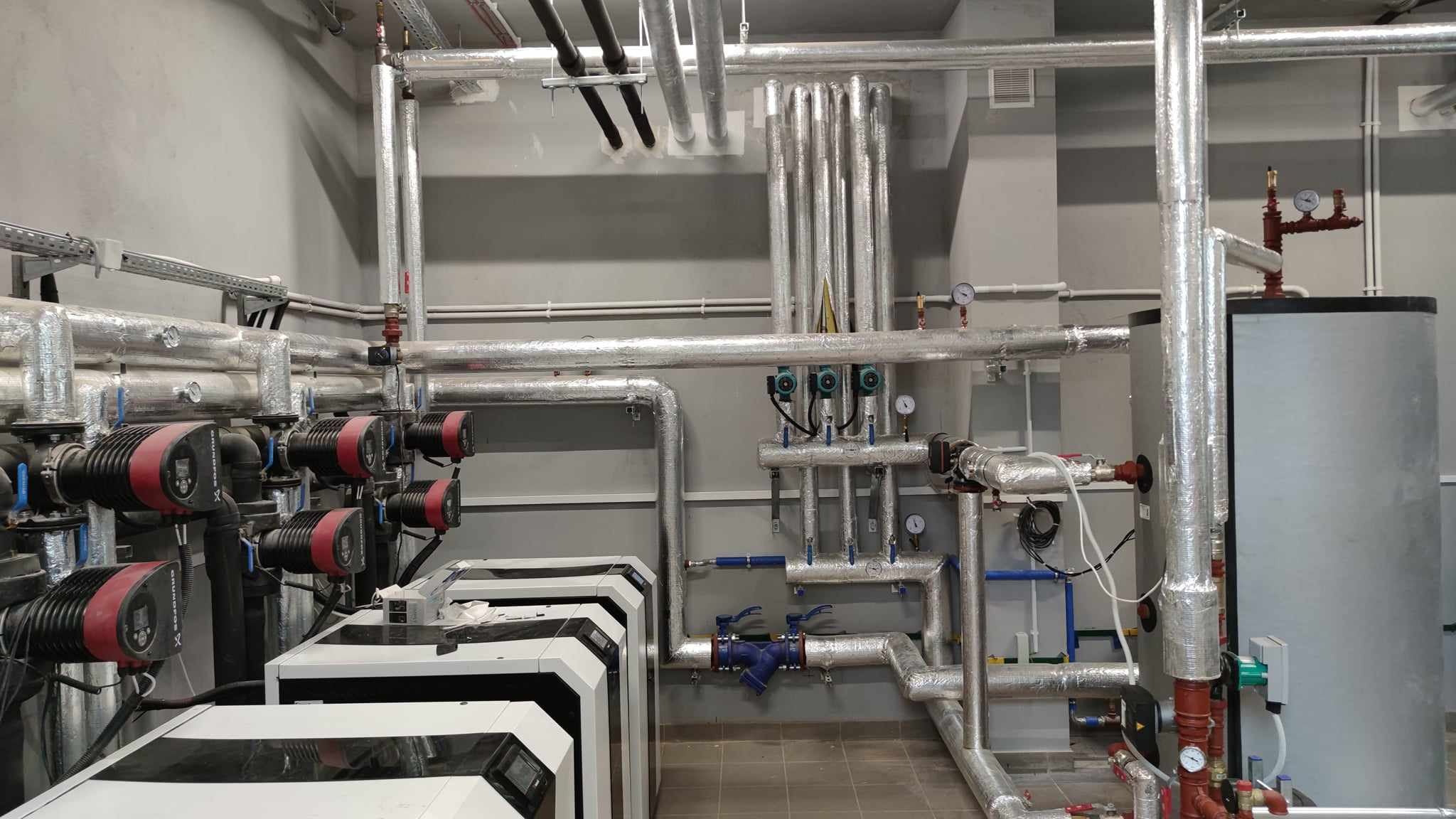 Instalacja grzewcza w kotłowni z izolowanymi rurami, pompami obiegowymi Grundfos i zbiornikiem akumulacyjnym.