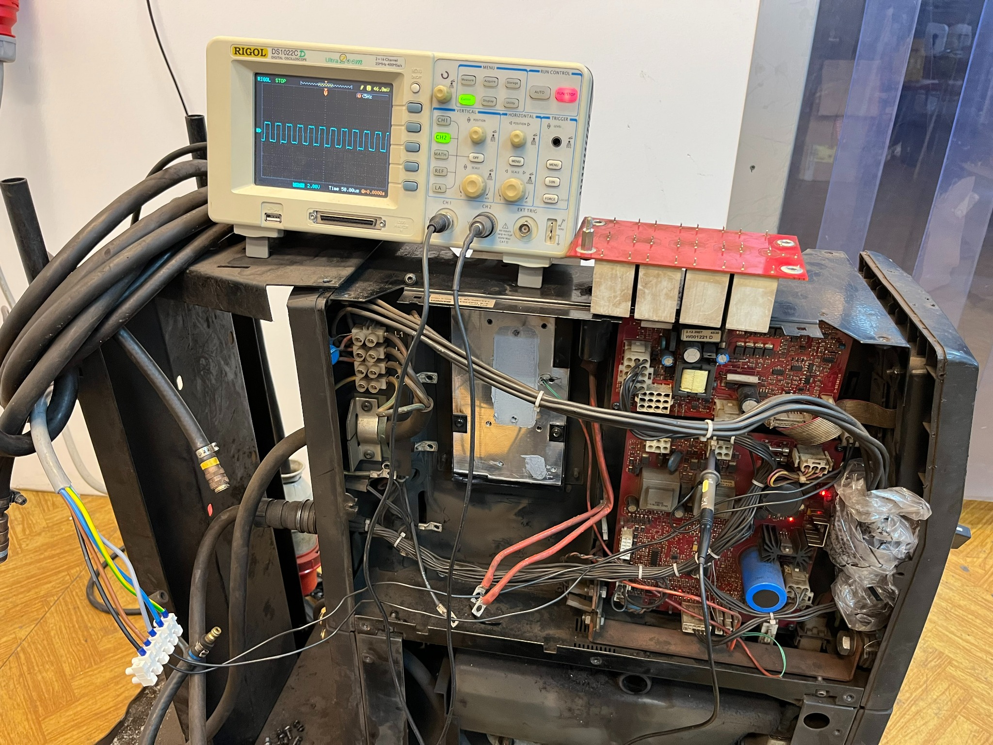 Oscyloskop Rigol wyświetlający przebieg sygnału podłączony do otwartej obudowy urządzenia z widoczną płytą elektroniki i okablowaniem.