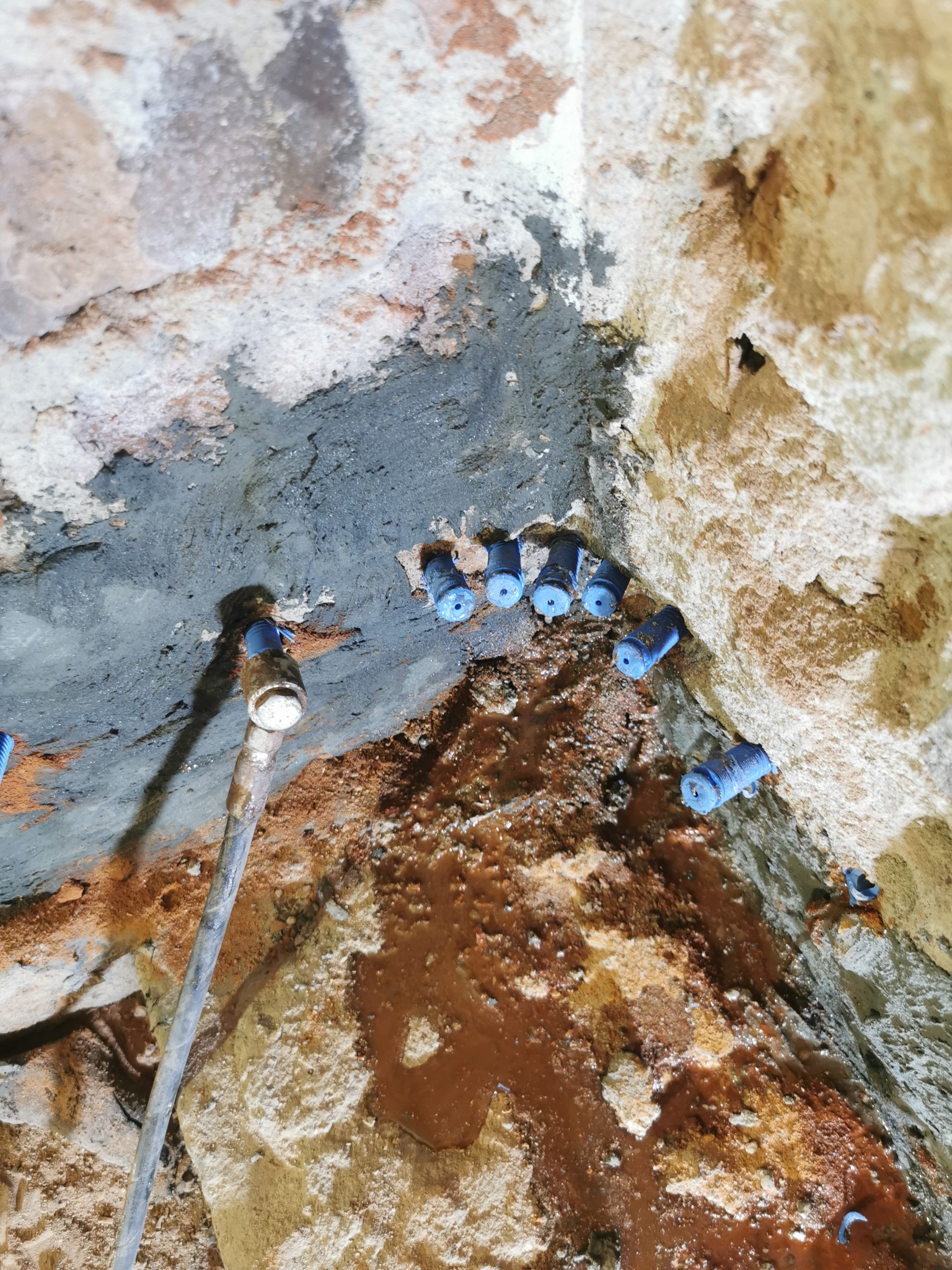 Wiercenie otworów w wilgotnej, ceglanej ścianie pod kątem, z widocznymi niebieskimi dyszami iniekcyjnymi i śladami wilgoci.