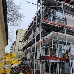 P&B Consulting Paweł Boniek - Budynek jednorodzinny w trakcie montażu stolarki okiennej i rolet zewnętrznych, widoczne rusztowania, materiały izolacyjne i elementy konstrukcyjne, pochmurne niebo w tle.