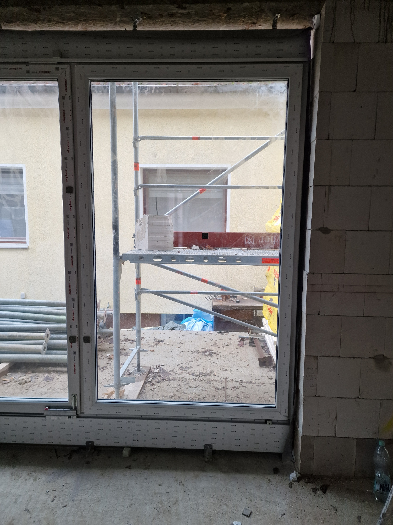 Wstawione okno Aluplast w surowym stanie, widoczne rusztowanie na zewnątrz budynku, niedokończone prace murarskie.