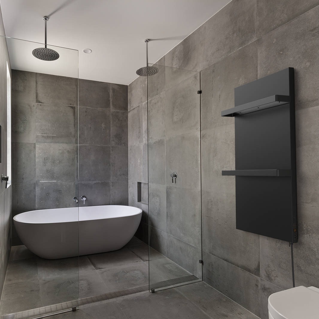 Nowoczesna łazienka z szarą, betonową okładziną ścienną, wolnostojącą białą wanną owalną, przeszkloną kabiną prysznicową z dwoma deszczownicami sufitowymi i czarnym, minimalistycznym grzejnikiem...