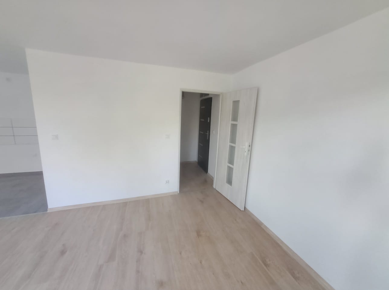 Jasne panele podłogowe w nowym, pomalowanym na biało pokoju z otwartymi drzwiami do kolejnego pomieszczenia.