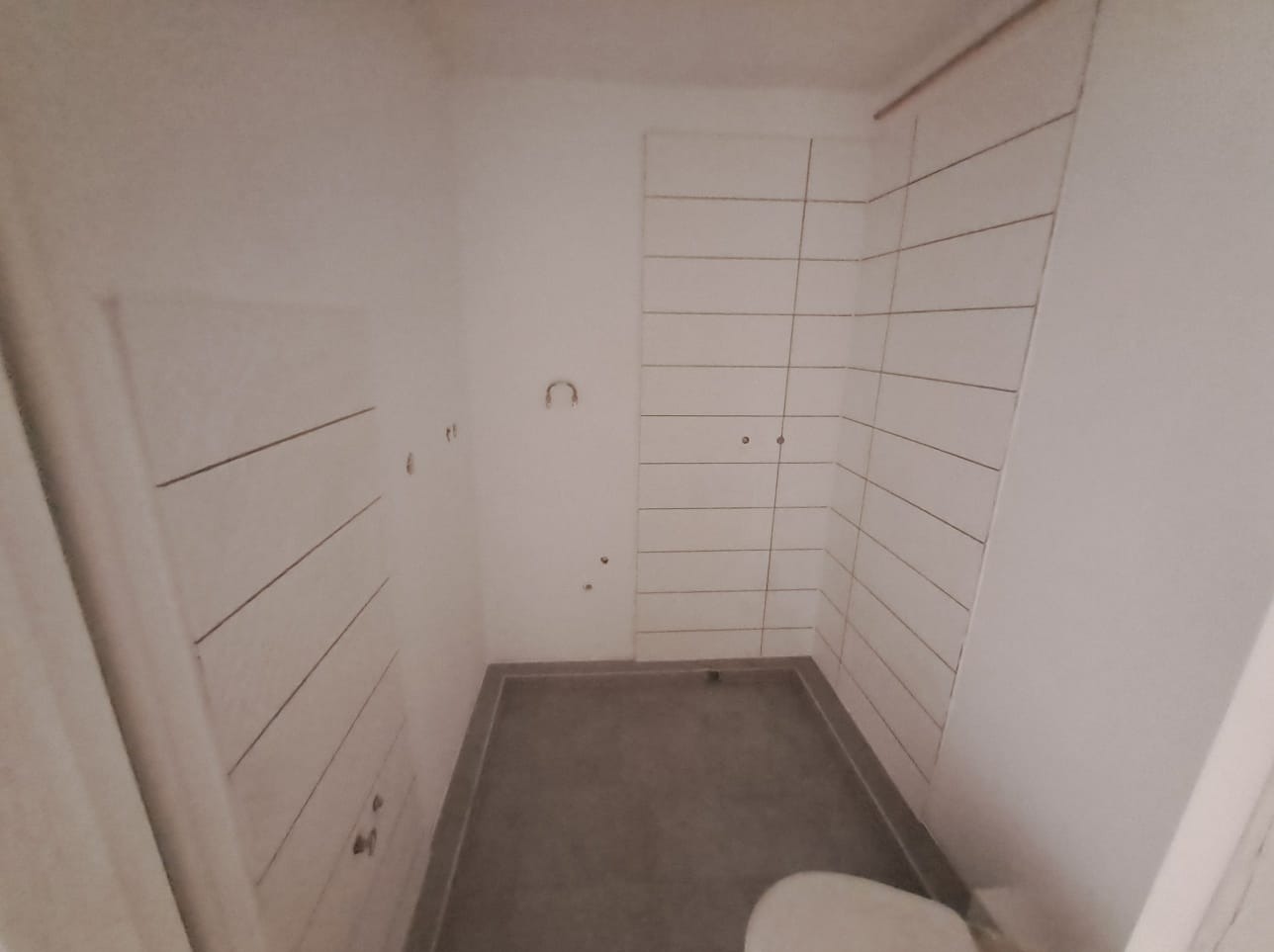 Wnętrze łazienki w trakcie remontu, z położonymi białymi, poziomymi płytkami na ścianie, przygotowaną podłogą i widocznymi instalacjami.