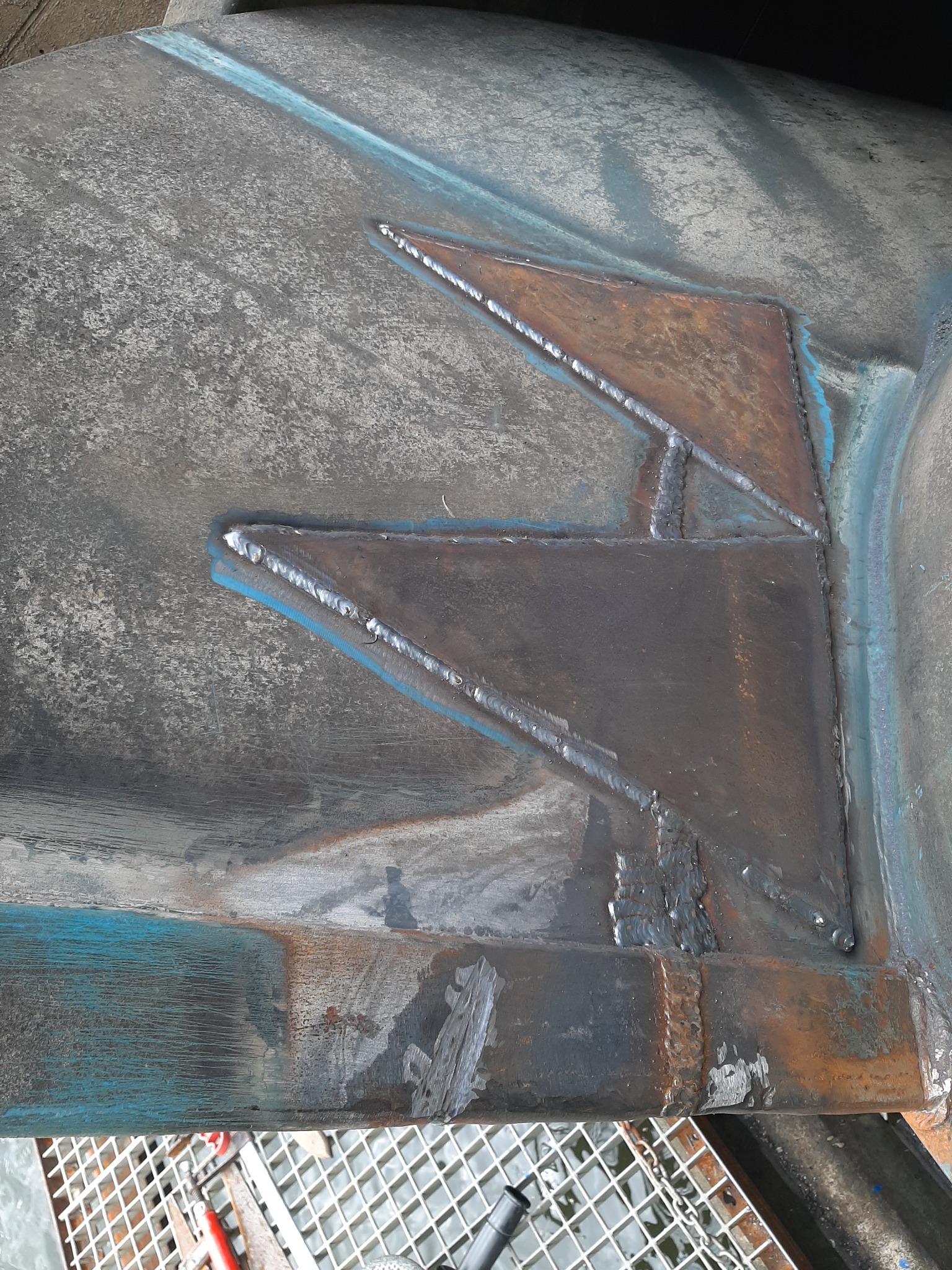 Szczegółowe ujęcie spawu na metalowej konstrukcji, widoczne ślady spawania i niebieska farba na powierzchni.