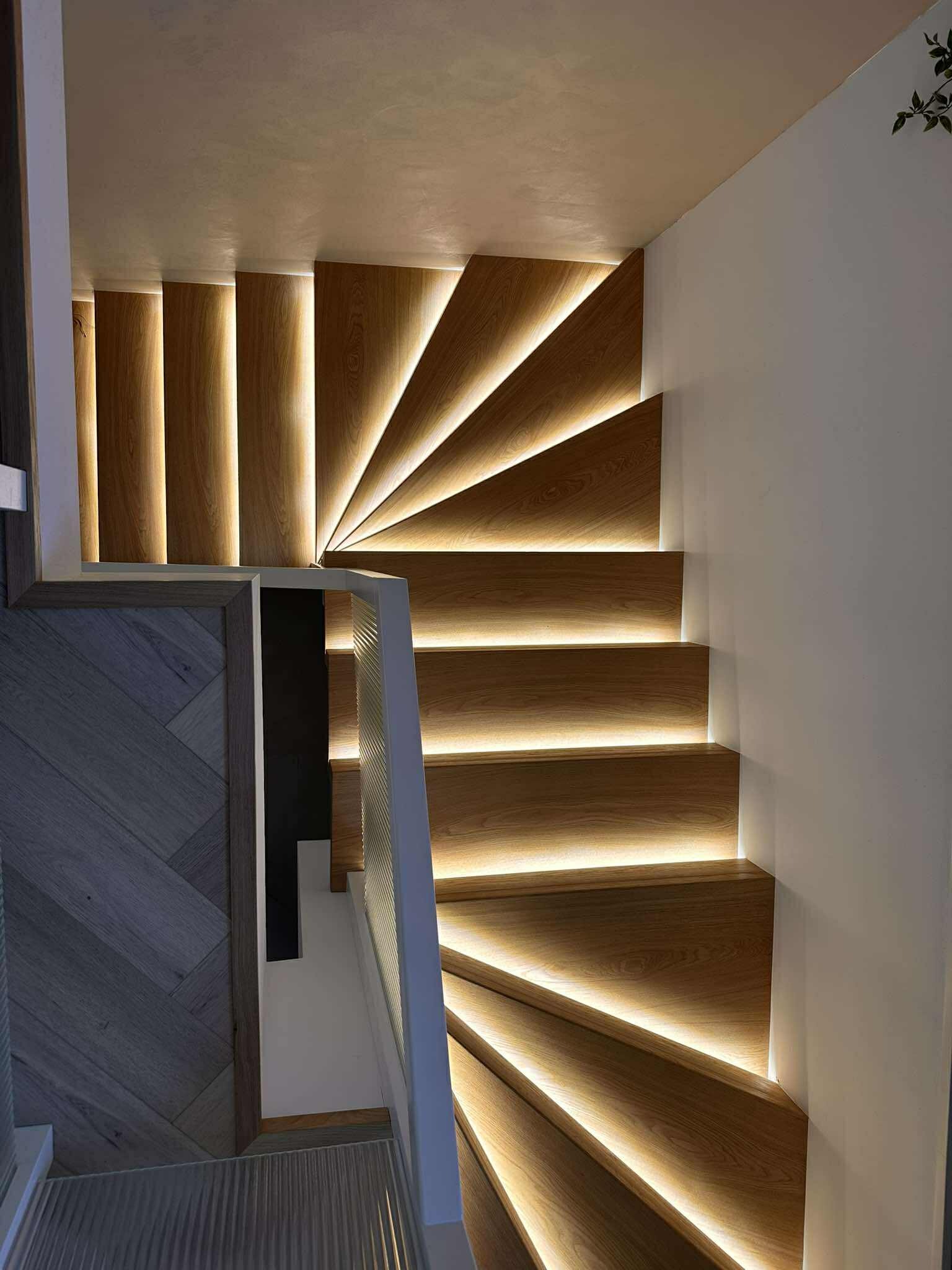 Nowoczesne schody z drewna z subtelnym podświetleniem LED, tworzące efektowny wizualnie element wnętrza. Ujęcie z góry podkreśla spiralny kształt i unikalny design.