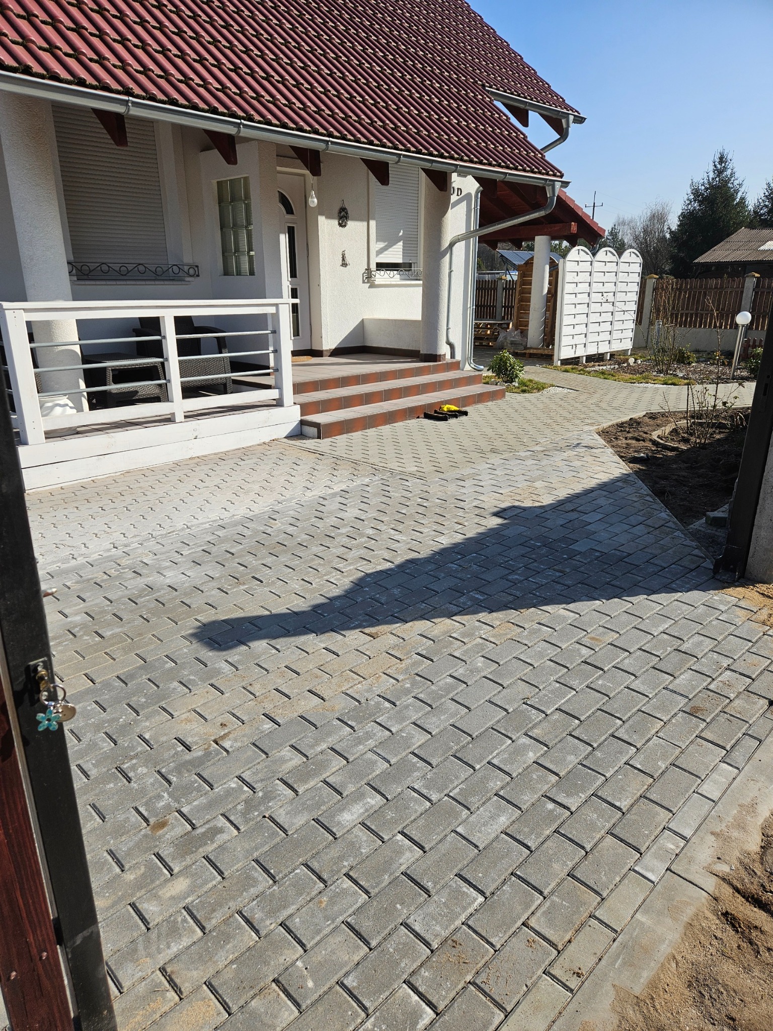 Nowo ułożona szara kostka brukowa prowadząca do domu z czerwonym dachem, widok zza furtki.