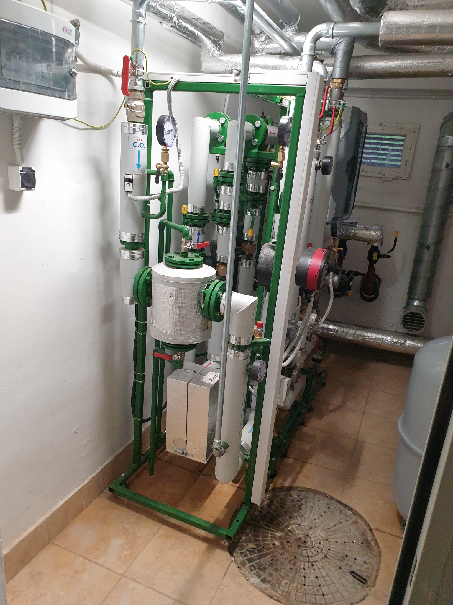 Instalacja grzewcza w kotłowni: rury, zawory, manometr, pompa obiegowa, filtr C.O., izolowane przewody, studzienka kanalizacyjna w podłodze.
