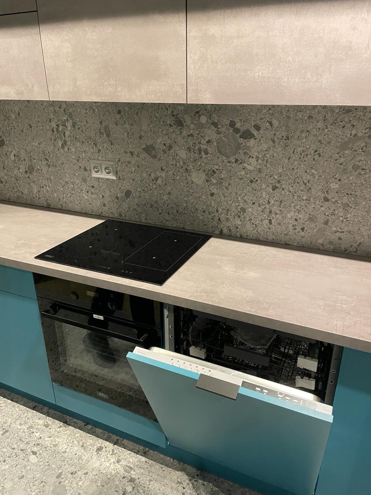 Nowoczesna kuchnia: turkusowe fronty szafek, szary blat i backsplash z motywem lastryko, płyta indukcyjna i otwarta zmywarka marki Kernau.
