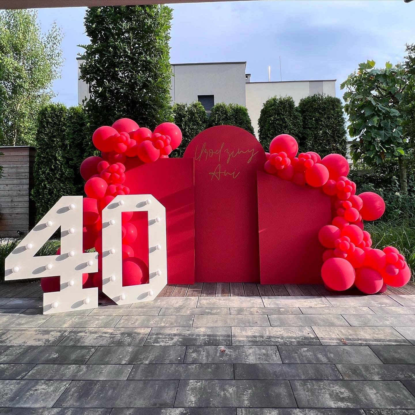 Dekoracja urodzinowa na 40 urodziny: czerwone panele z napisem 'Urodziny Ani', białe podświetlane cyfry '40' i girlanda z czerwonych balonów na zewnątrz.