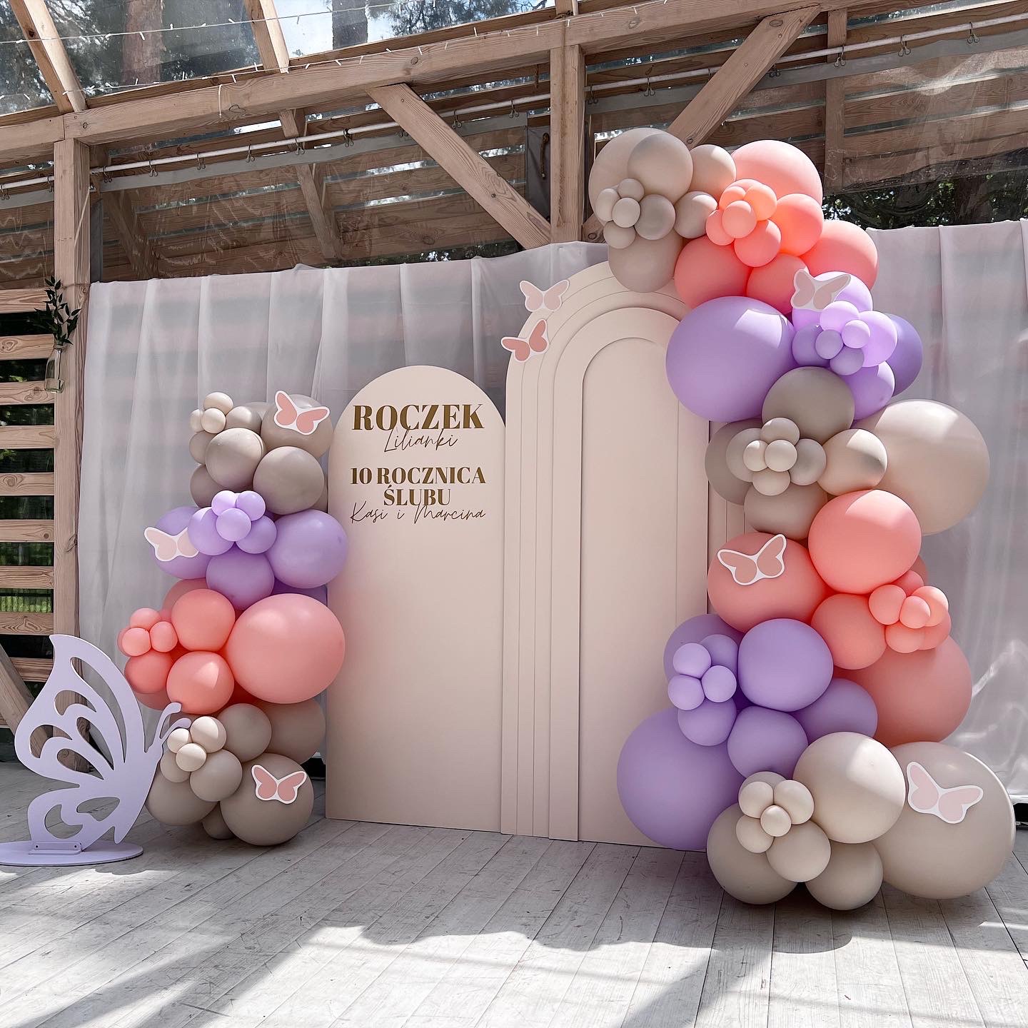 Pastelowa dekoracja balonowa z motywem motyli na roczek i 10 rocznicę ślubu, ustawiona na drewnianej podłodze.
