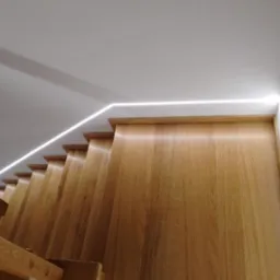 Oświetlenie LED liniowe zamontowane wzdłuż schodów drewnianych, widok od dołu, ciepła barwa światła.