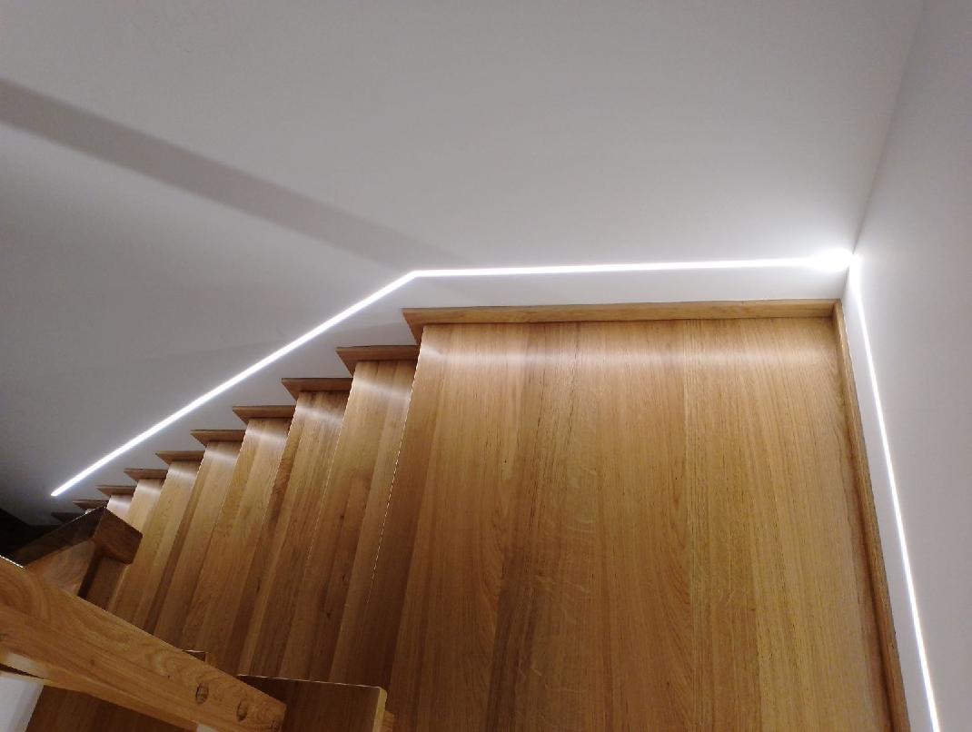 Oświetlenie LED liniowe zamontowane wzdłuż schodów drewnianych, widok od dołu, ciepła barwa światła.