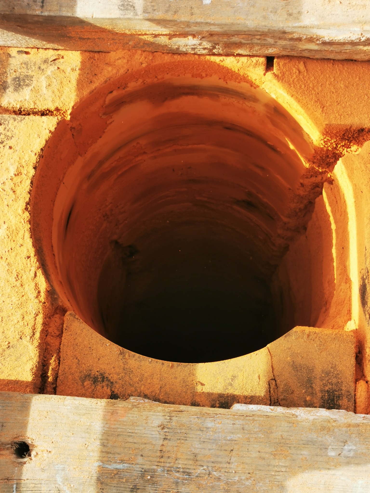 Otwór kominowy wyłożony cegłą szamotową w Pszczynie, widok z góry na ciemne wnętrze przewodu kominowego, drewniane elementy konstrukcyjne wokół.