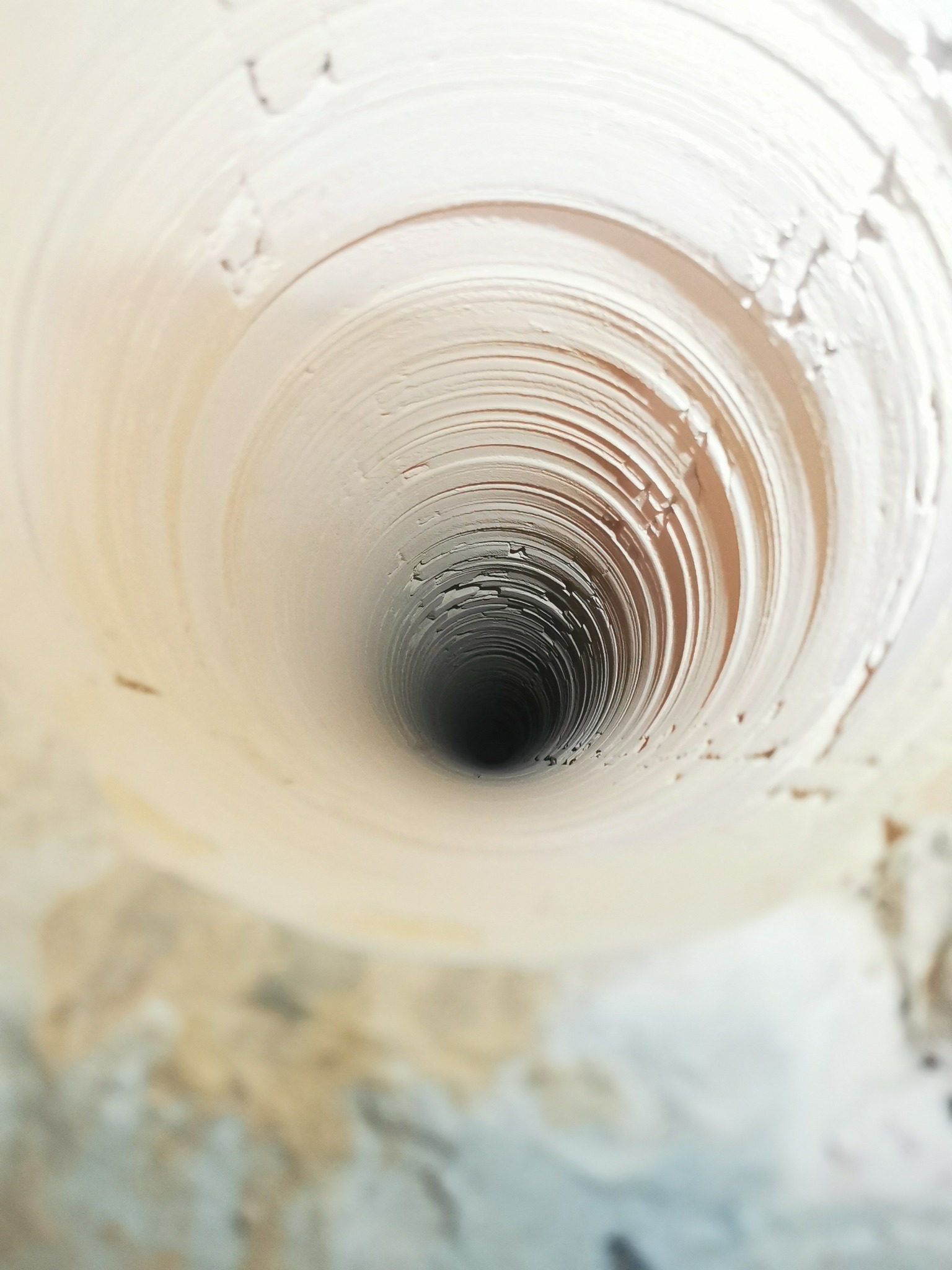 Wnętrze ceramicznego przewodu kominowego z widocznymi śladami po czyszczeniu, skierowane w dół, z ciemnym otworem na końcu.