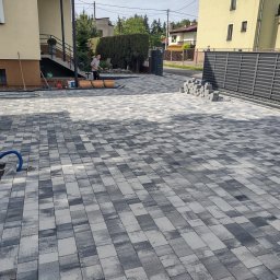 Mateusz Kubiczek - Ułożona kostka brukowa w odcieniach szarości przed domem z widocznym fragmentem posesji i przygotowanymi materiałami do dalszych prac.