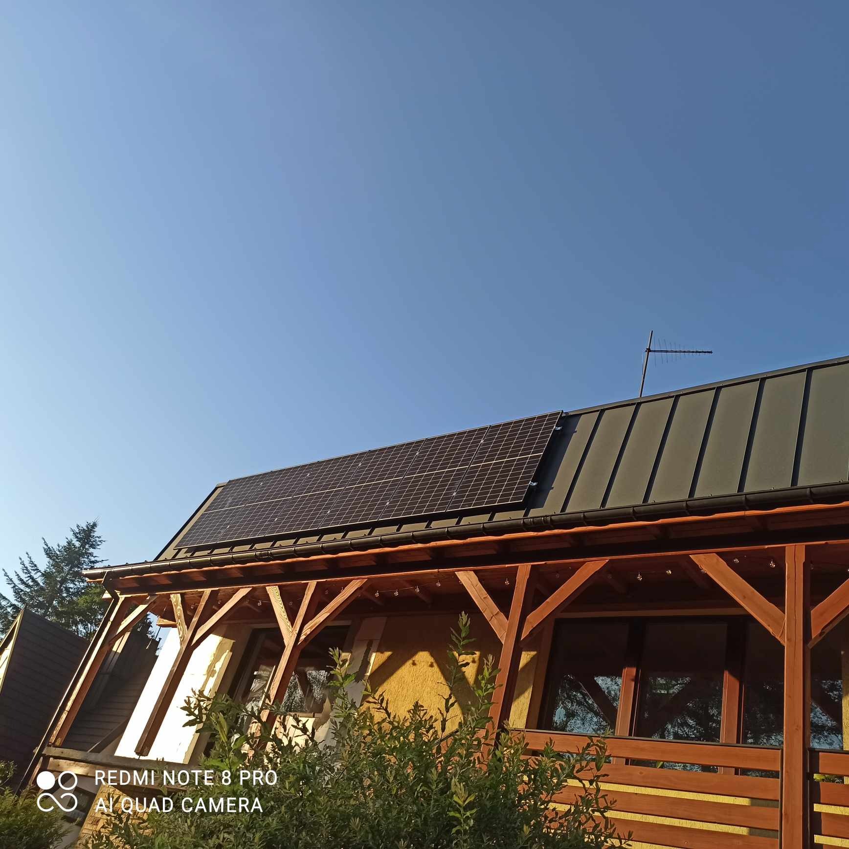 Panele słoneczne zamontowane na dachu domu z drewnianą konstrukcją werandy w słoneczny dzień.