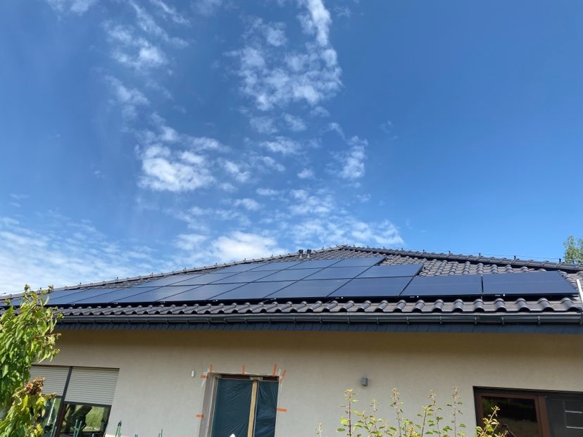 Panele słoneczne na dachu domu jednorodzinnego z ciemną dachówką, widok z dołu w słoneczny dzień, okno zabezpieczone folią.