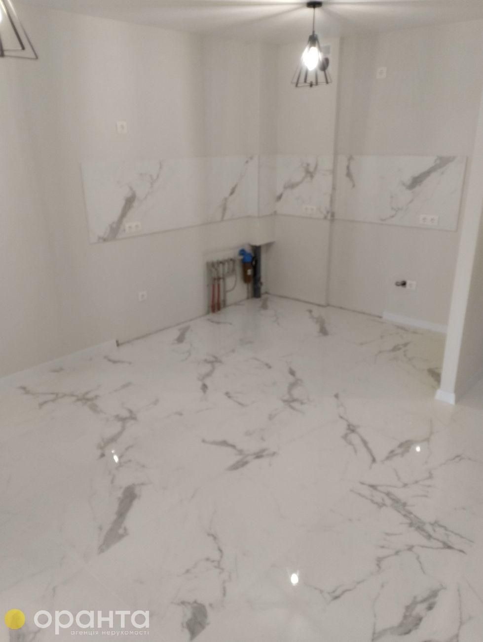 Wykończona łazienka z białymi płytkami imitującymi marmur na podłodze i ścianie nad instalacją hydrauliczną. Nowoczesne oświetlenie sufitowe.