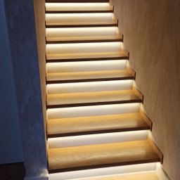 Piotr Słomka - Schody drewniane z podświetleniem LED na każdym stopniu, oświetlające klatkę schodową w ciepłym, jasnym odcieniu.